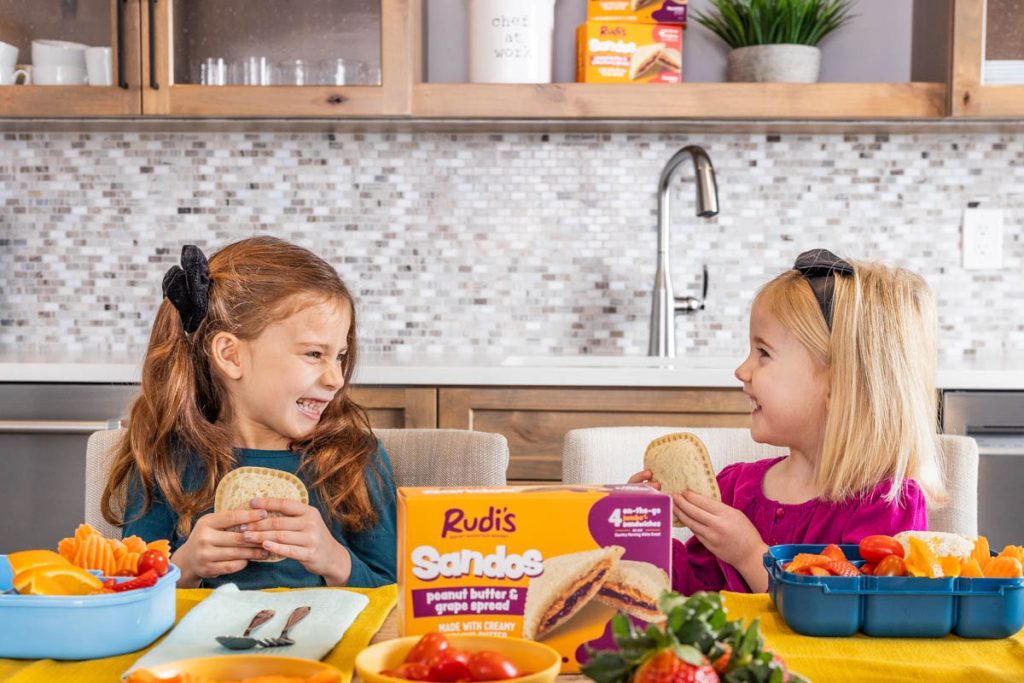 two kids eating Rudi's Sandos at the kitchen table